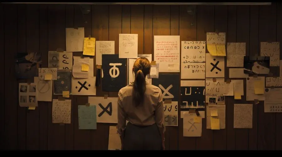 Maika Monroe faces a wall plastered with papers in the film Longlegs