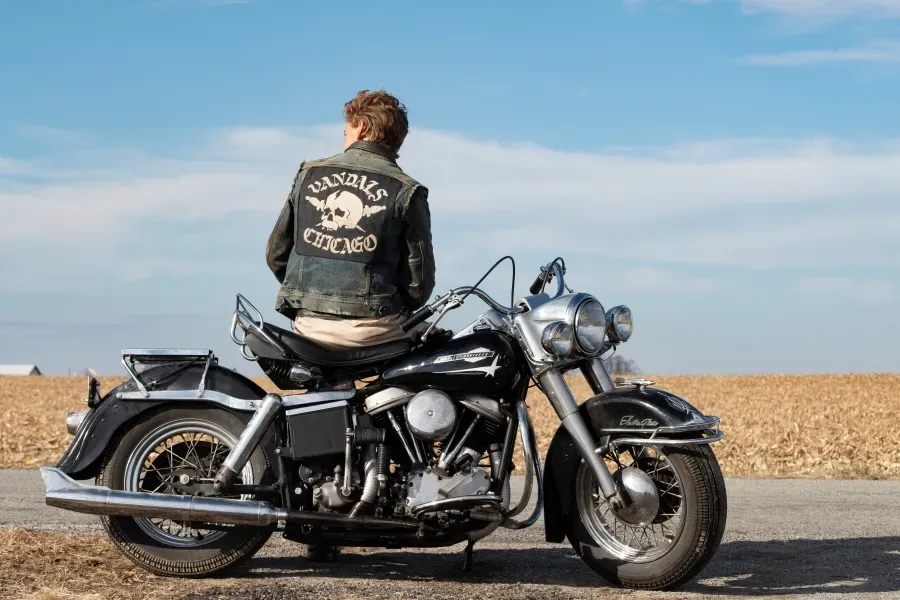 Austin Butler sitting on a motorcycle against a grain field in the film The Bikeriders